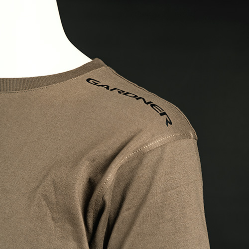 A close-up of a green T-shirt worn by a mannequin, showing the back and shoulder with the word GARDNER printed in black on the shoulder area against a plain dark background.