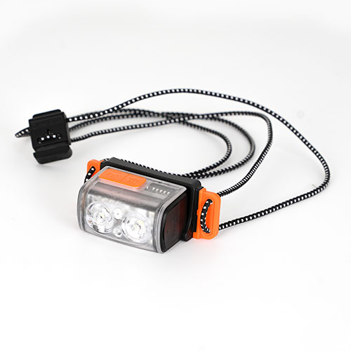 The Tiny Helio Headtorch features three LED lights, an orange button, and an adjustable black-and-white elastic strap, shown against a white background.